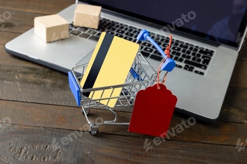 Preview: Composition of shopping cart with credit card and laptop on wooden background