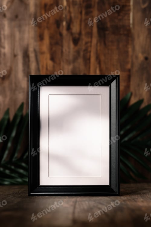 Preview: blank black photo frame on wood table and wall witn sunlight from window