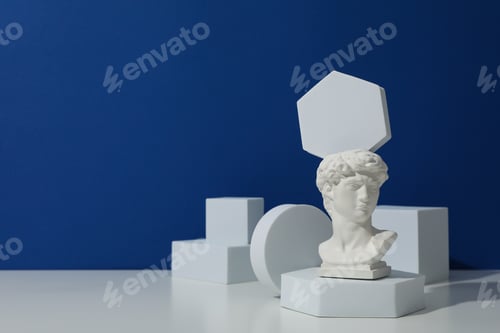 Preview: Geometric figures and ancient head on white table against blue background