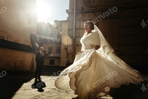 Preview: happy gorgeous bride and stylish handsome groom dancing on background of old buildings