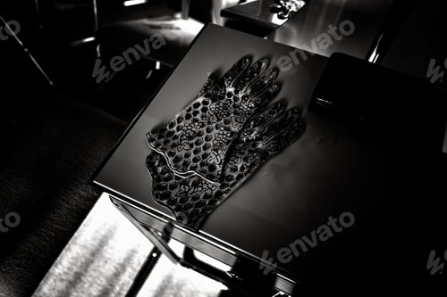 Preview: Pair of ornate black gloves with a detailed pattern on a table in grayscale