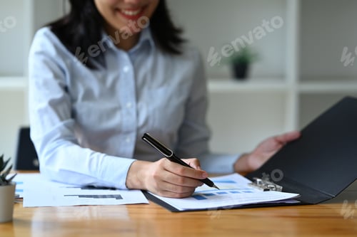 Preview: Cropped shot of female manager signing contract at office desk.