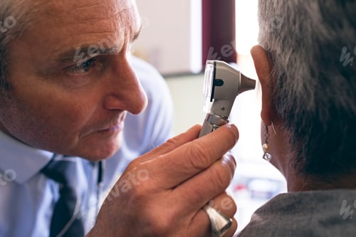 Preview: Middle section of matured male doctor checking senior African American female patient in clinic