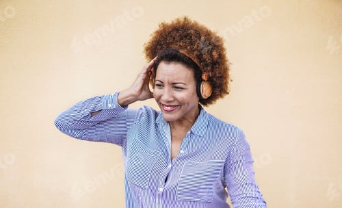 Preview: Beautiful mature african woman listening music with wireless headphone