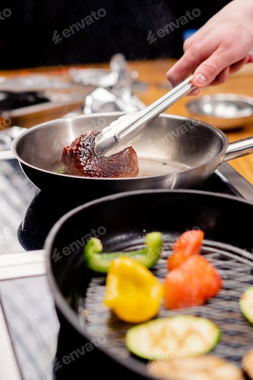 Preview: close-up of seared beef steak with rosemary in tongs on frying pan next to vegetables