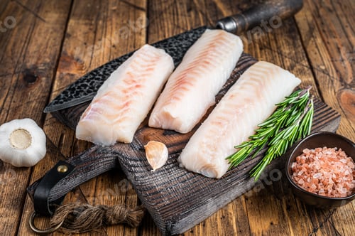 Preview: Fresh Raw cod loin fillet steaks on wooden board with butcher knife. wooden background. Top view