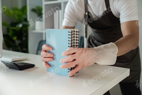 Preview: Person Cleaning Desk with Gloves and Organizing Notebooks in a Modern Office Environment