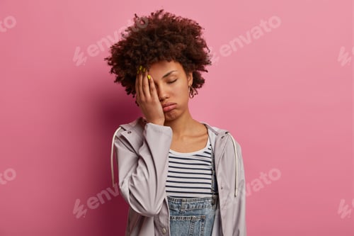 Preview: Portrait of tired bored young woman feels lazy and disinterested, coves face with palm, has gloomy f