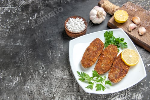 Preview: bottom view cutlets lemon slices parsley on white plate garlic bowl of sea salt cutting board on