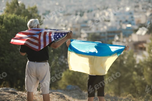 Preview: Retired man and kid boy holding the flags of the USA and Ukraine on city view