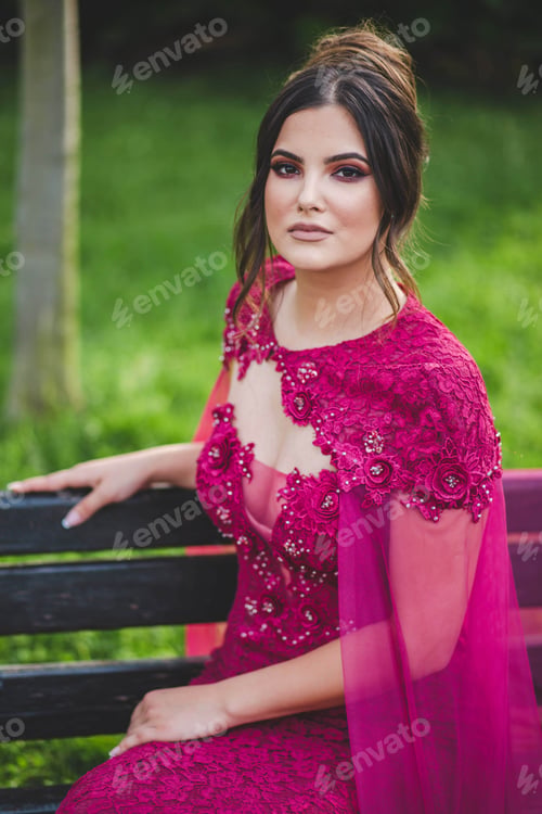Preview: Vertical shot of a beautiful Caucasian female with pink dress sitting on a bench