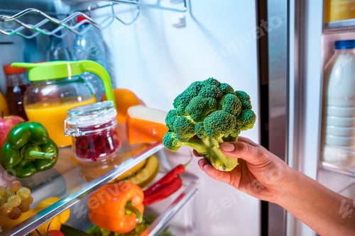 Preview: Woman takes the broccoli from the open refrigerator.