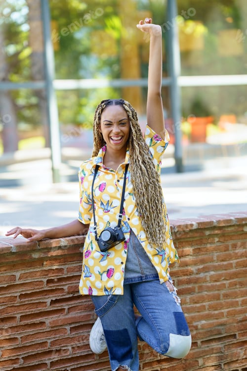 Preview: Black woman with African braids, raising her arm in joy. Girl holding a camera.