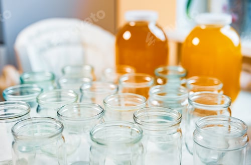 Preview: Composition of a large number of jars and three jars of honey standing on a white table against a
