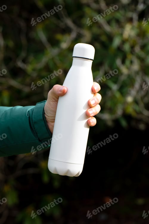 Preview: man holds mockup thermos against blurry bushes closeup