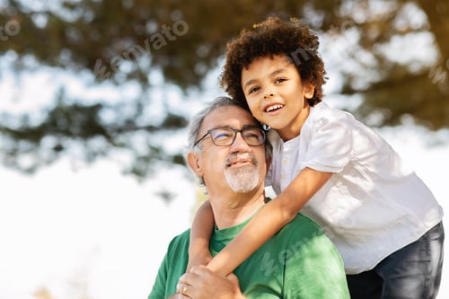 Preview: Happy glad senior man with beard and black little boy hugging, have fun in park, enjoy weekend