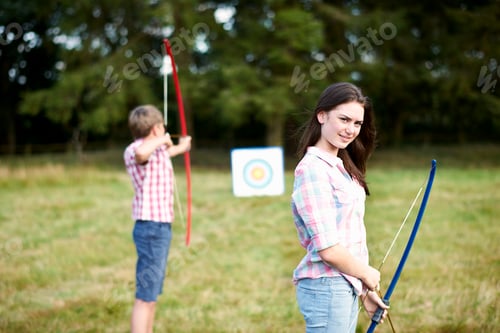 Preview: Portrait of teenage girl practicing archery with brother