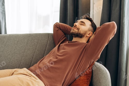 Preview: Smiling, handsome Hispanic man relaxing, lying on comfortable sofa in cozy home. Resting concept