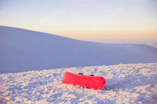 Preview: A vibrant red snowboard rests on a snowy mountain slope at sunset.