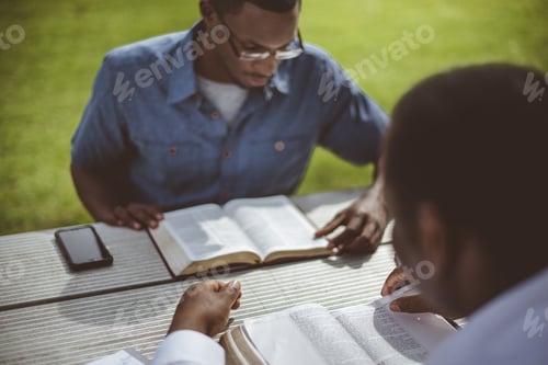 Preview: African-American male friends sitting at the table and reading the Bible at the table