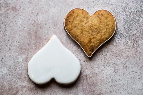 Preview: High angle close up of two freshly baked hart-shaped cookies decorated with white icing.