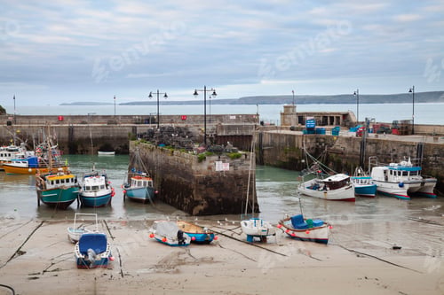 Preview: Low tide at a Cornish harbour, sea coast fishing village, boats moored, beached on the sand.