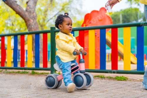 Preview: African baby girl riding a toy bike in a park