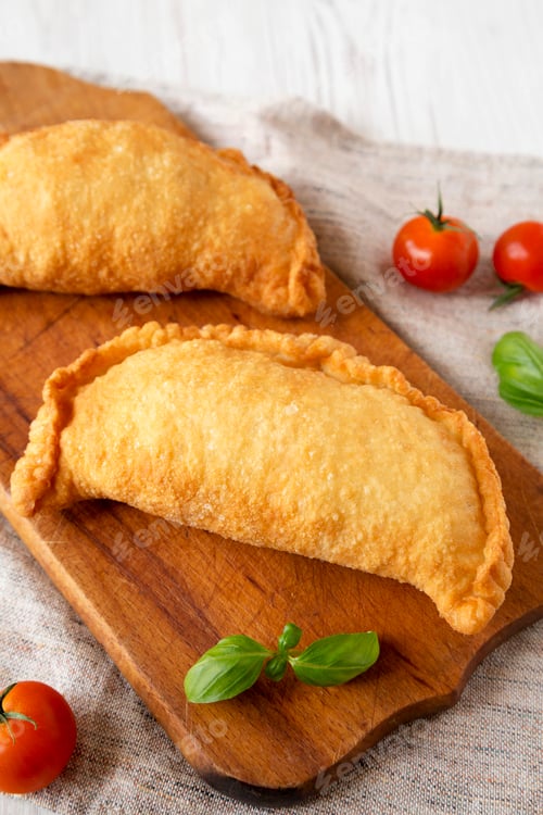 Preview: Homemade Deep Fried Italian Panzerotti Calzone on a rustic wooden board on a white wooden table