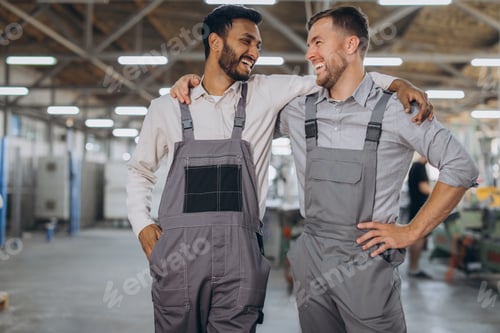 Preview: Two happy international workers in overalls hug each other against a factory background