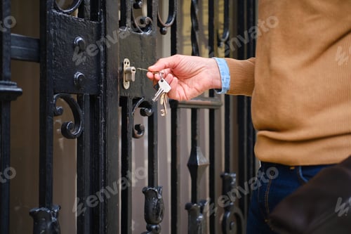 Preview: side view of adult Man opening home gate with keys. unrecognizable person