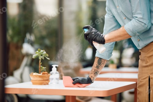 Preview: Close-up of waiter cleaning tables and spraying them with disinfectant during coronavirus pandemic,