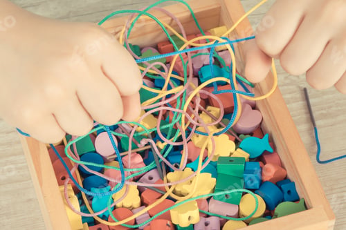 Preview: Hands of kid playing thread and colorful beads used to making bracelets