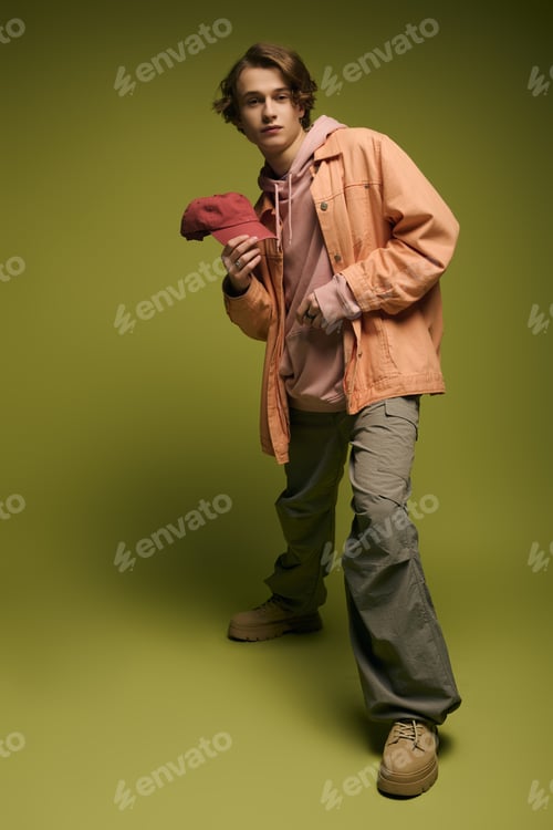 Preview: Young man showcases trendy attire with a stylish cap against a vibrant green backdrop