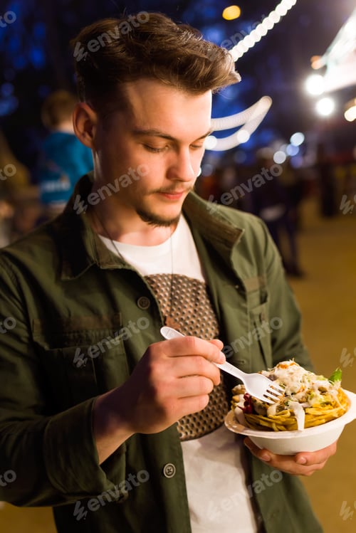 Preview: Handsome young man eating chips in the street.