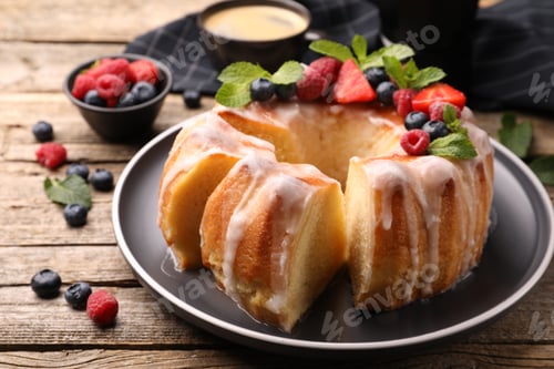 Preview: Pieces of delicious bundt cake with berries, glaze and mint on wooden table, closeup