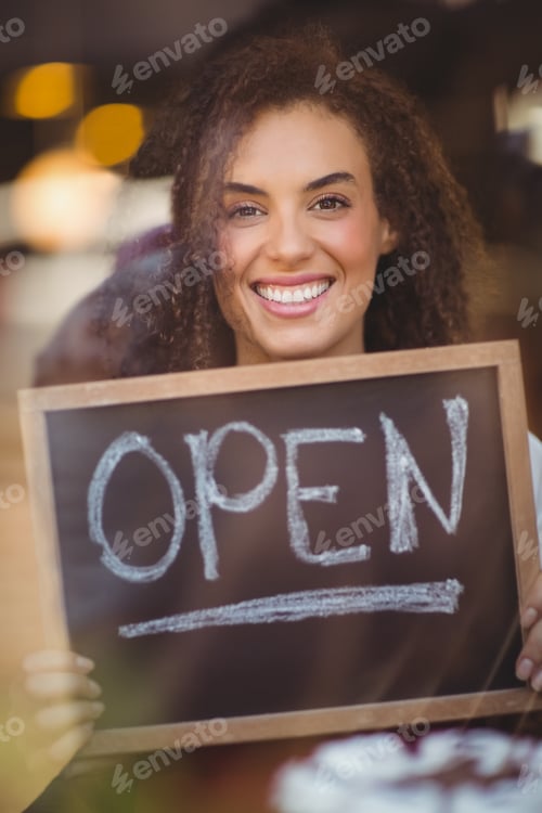 Preview: Portrait of a waitress showing chalkboard with open sign at the coffee shop