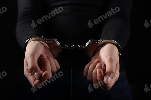 Preview: Woman in metal handcuffs on black background, closeup