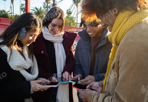 Preview: Group of diverse friends in winter clothes browsing the internet with smart phone in the city.