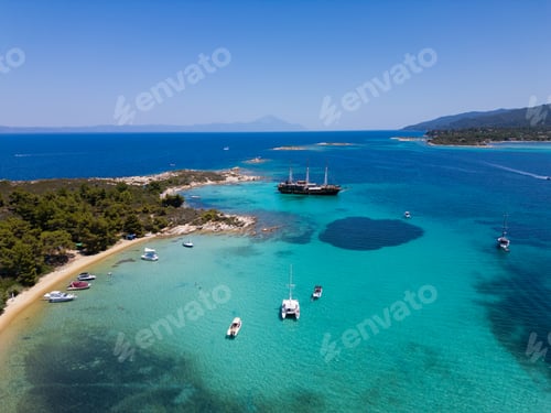 Preview: Aerial view of a coastal landscape with turquoise waters, sandy beaches, and a sailing ship anchored