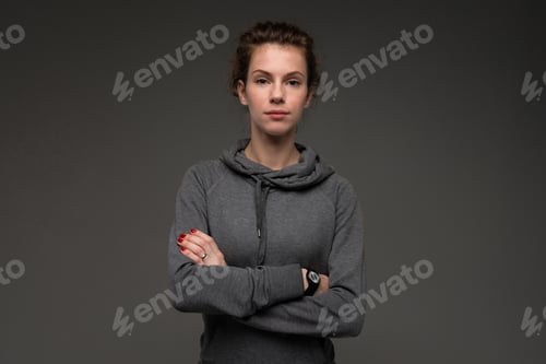Preview: attractive caucasian girl in a gray sweatshirt with arms crossed on a black background