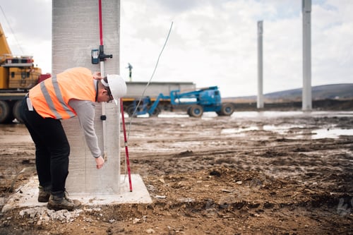 Preview: industrial engineer working on building site with cement pillars and surveying tools