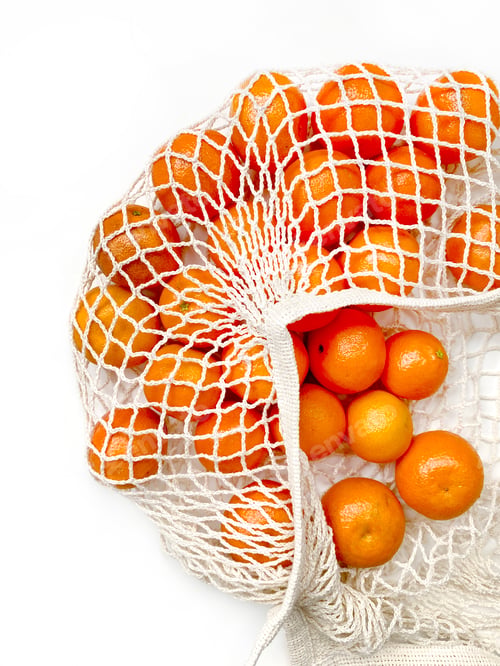 Preview: Mesh bag of fresh oranges healthy citrus fruits from on white background. Flat lay, top view.