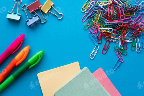 Preview: top view of colorful paper clips and fold back clips near paper notes on blue