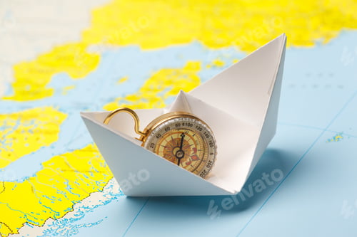Preview: Compass on a paper boat positioned on a map showing water and land areas in bright colors