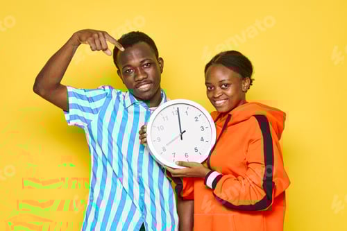 Preview: Young couple of african appearance holding a watch in yellow hands