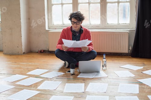 Preview: Young man sitting on the floor in a rehearsal studio, using a laptop computer, looking at sheet
