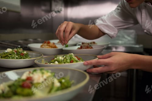 Preview: Female chef garnishing appetizer plates at order station