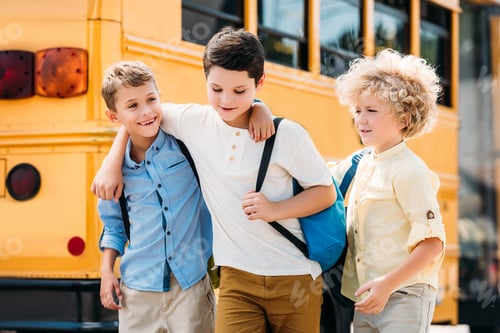 Preview: happy little schoolboys having fun together in front of school bus