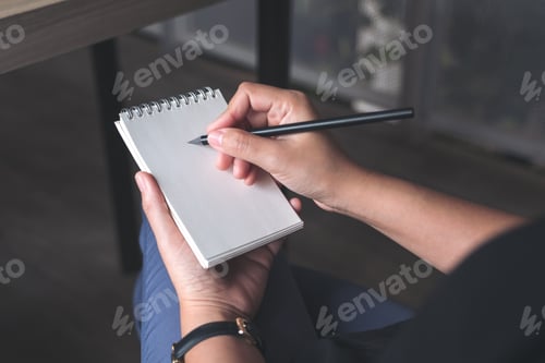 Preview: Closeup image of a woman's hands writing down on a white blank notebook