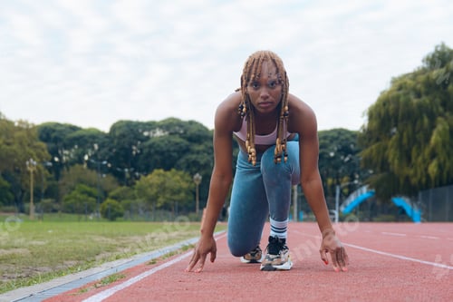 Preview: young female athlete at the starting line on the running track